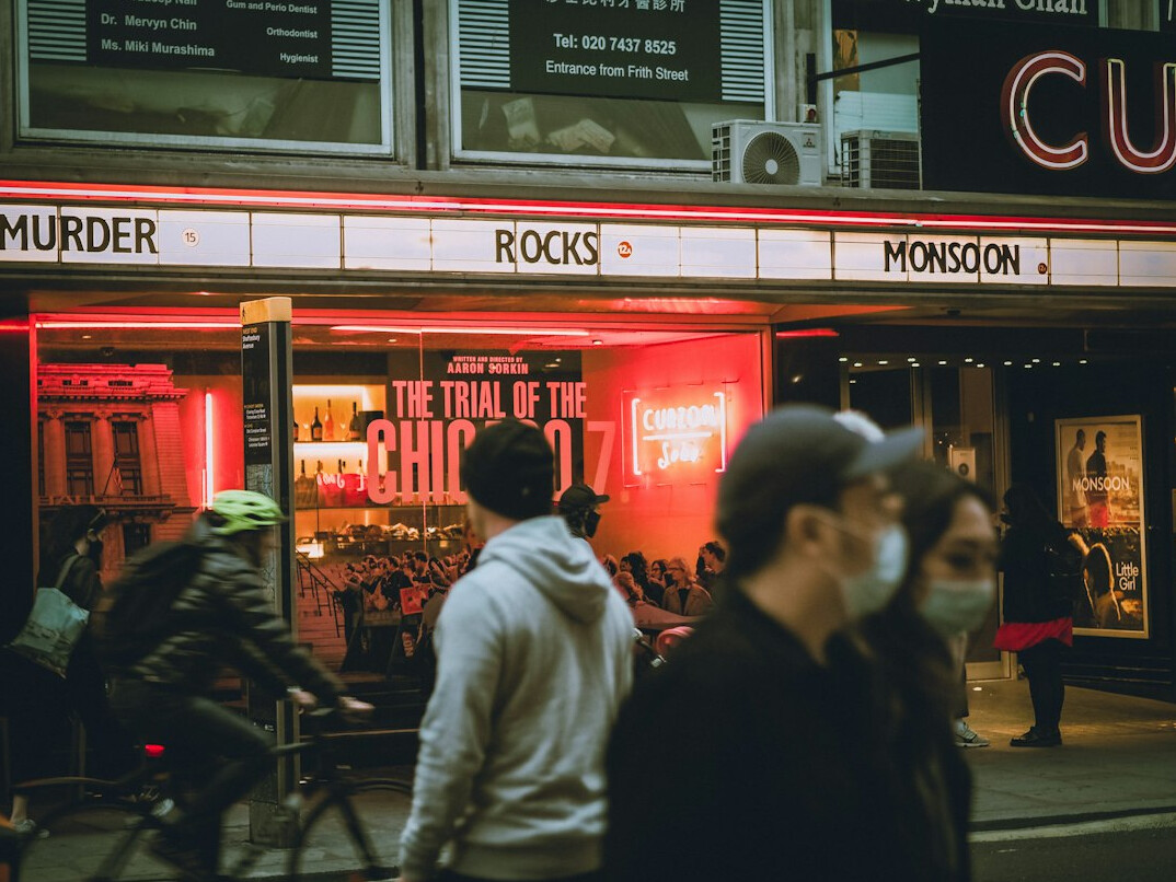 People queueing outside a cinema at dusk with a neon sign
